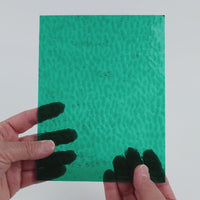 Video of the Teal Hammered glass plate in hammered transparent teal, 15x19cm, held up and tilted to show its pattern and transparency