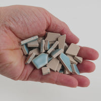 Video of Flip ceramic puzzle pieces in ice blue, opaque glazed porcelain, 4–20 mm, held in a hand and poured out to show their shapes and finish