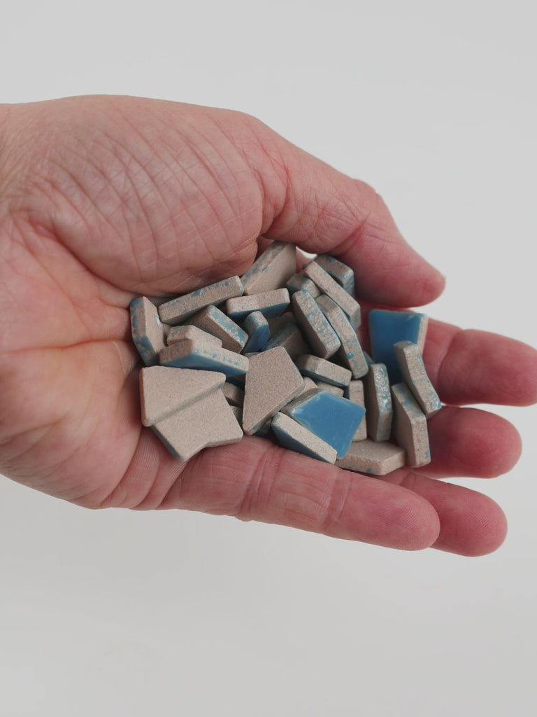 Video of Flip ceramic puzzle pieces in Caribbean blue, opaque glazed porcelain, 4–20 mm, held in a hand and poured out to show their shapes and finish