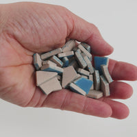 Video of Flip ceramic puzzle pieces in Caribbean blue, opaque glazed porcelain, 4–20 mm, held in a hand and poured out to show their shapes and finish