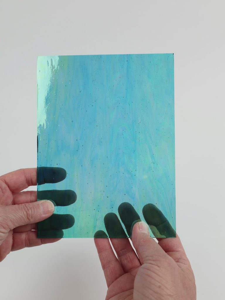 Video of the Teal iridised glass plate in iridescent transparent teal, 15x19cm, held up and tilted to show its pattern and transparency