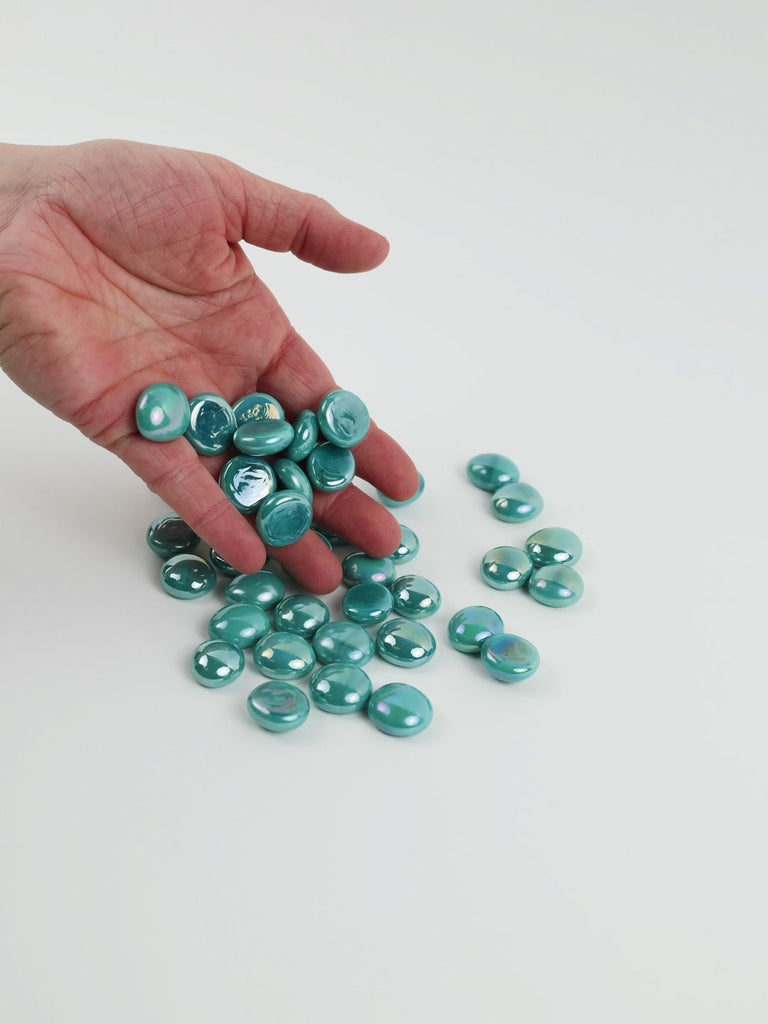 Video of opal cyan glass nuggets, opaque with a pearly iridescent sheen, 16–20 mm, picked up from a pile by hand and dropped back to show their size, round shape and shine