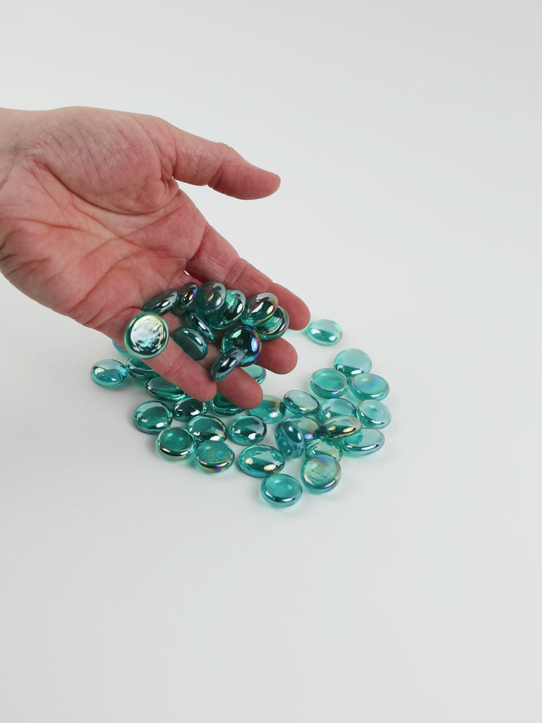Video of diamond cyan glass nuggets, transparent with an iridescent sheen, 16–20 mm, picked up from a pile by hand and dropped back to show their size, round shape and shine