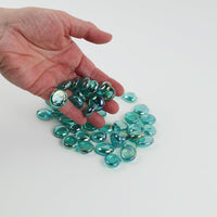 Video of diamond cyan glass nuggets, transparent with an iridescent sheen, 16–20 mm, picked up from a pile by hand and dropped back to show their size, round shape and shine