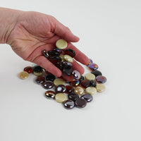 Video of caramel mix glass nuggets in dark brown, amber and cream shades with an iridescent sheen, 16–20 mm, picked up from a pile by hand and dropped back to show their size, round shape and shine