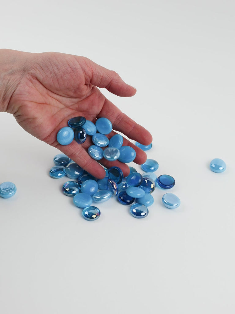 Video of turquoise mix glass nuggets in sky blue and turquoise shades with an iridescent sheen, 16–20 mm, picked up from a pile by hand and dropped back to show their size, round shape and shine