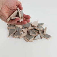 Video of Flip XL ceramic puzzle pieces in smoke grey, opaque glazed porcelain, 20–60 mm, picked up from a pile by hand and dropped back to show their size, shapes and finish
