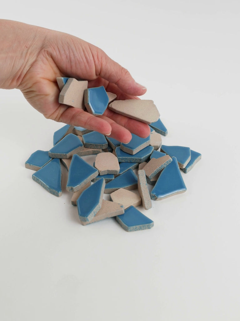 Video of Flip XL ceramic puzzle pieces in Caribbean blue, opaque glazed porcelain, 20–60 mm, picked up from a pile by hand and dropped back to show their size, shapes and finish