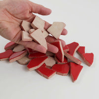 Video of Flip XL ceramic puzzle pieces in cherry red, opaque glazed porcelain, 20–60 mm, picked up from a pile by hand and dropped back to show their size, shapes and finish